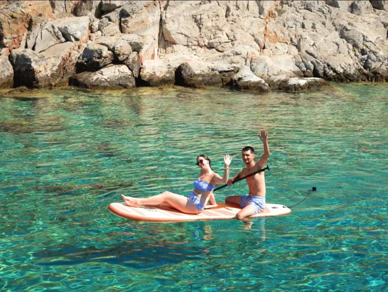 couple sitting on a surf-board in the sea near the rocky shore